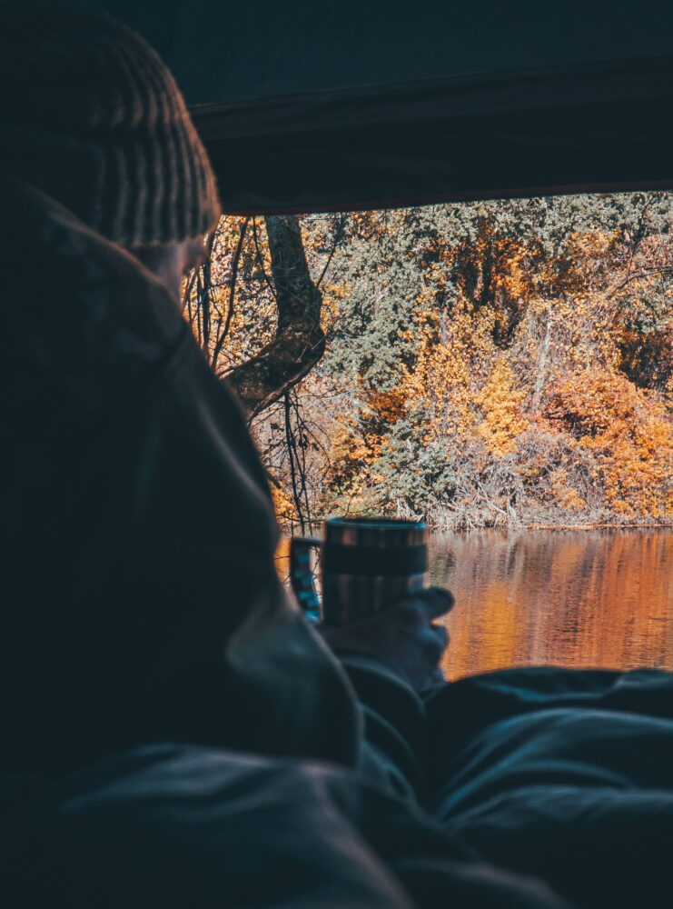 person sips a mug in the back of a van overlooking an autumnal landscape