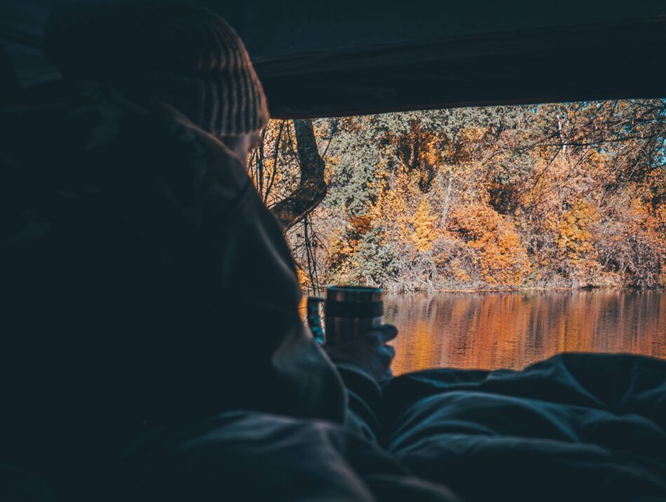 person sips a mug in the back of a van overlooking an autumnal landscape