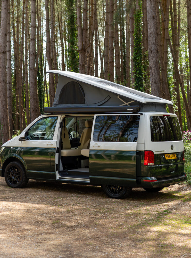 Green and white two-toned campervan with pop-top in woodland from rear